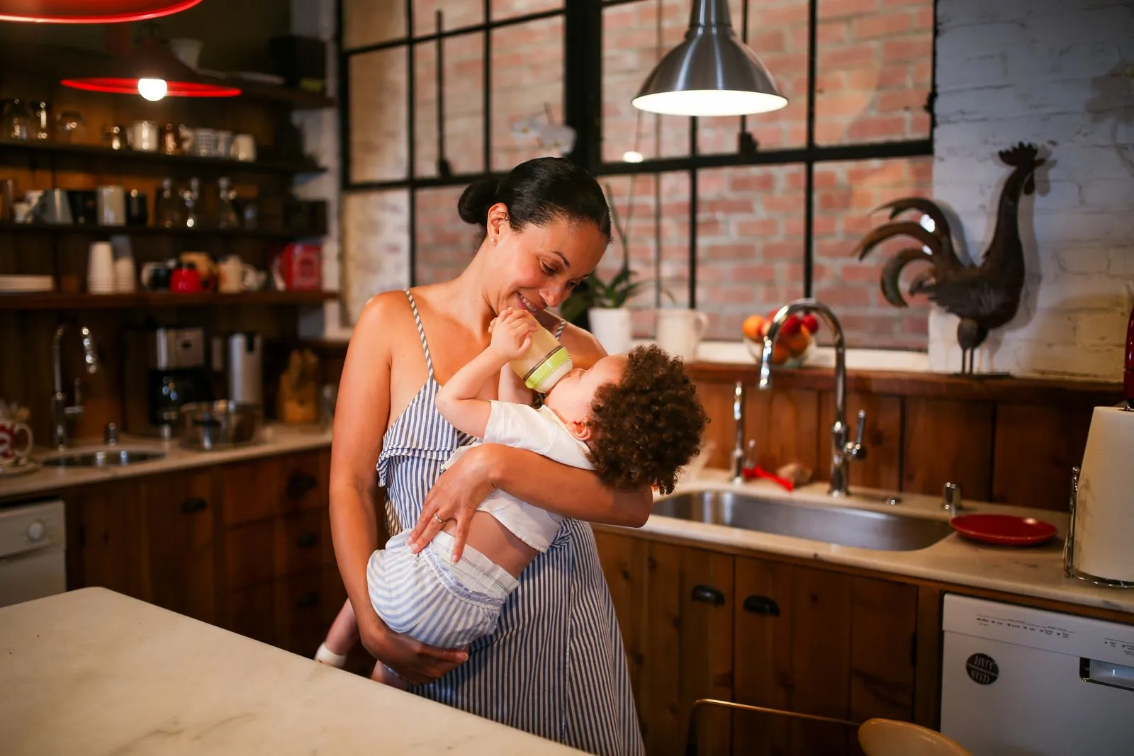 A loving mother feeding her baby with a bottle in a warm, rustic kitchen.